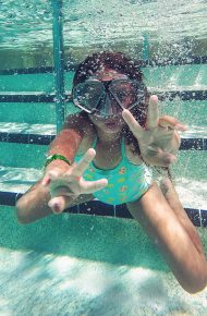 Ragazza sotto l’acqua di una piscina che saluta